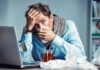 Man with tissue feeling unwell at laptop desk