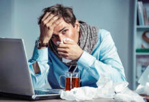 Man with tissue feeling unwell at laptop desk