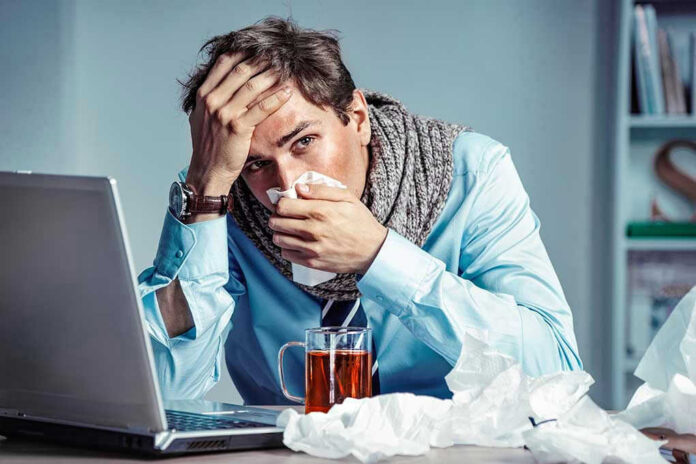 1112983769 Man with tissue feeling unwell at laptop desk