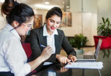 Two women discussing papers at a laptop