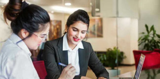 Two women discussing papers at a laptop