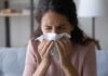 Woman sneezing into a tissue indoors