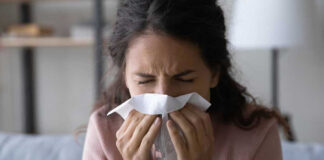 Woman sneezing into a tissue indoors
