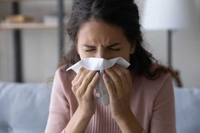 Woman sneezing into a tissue indoors